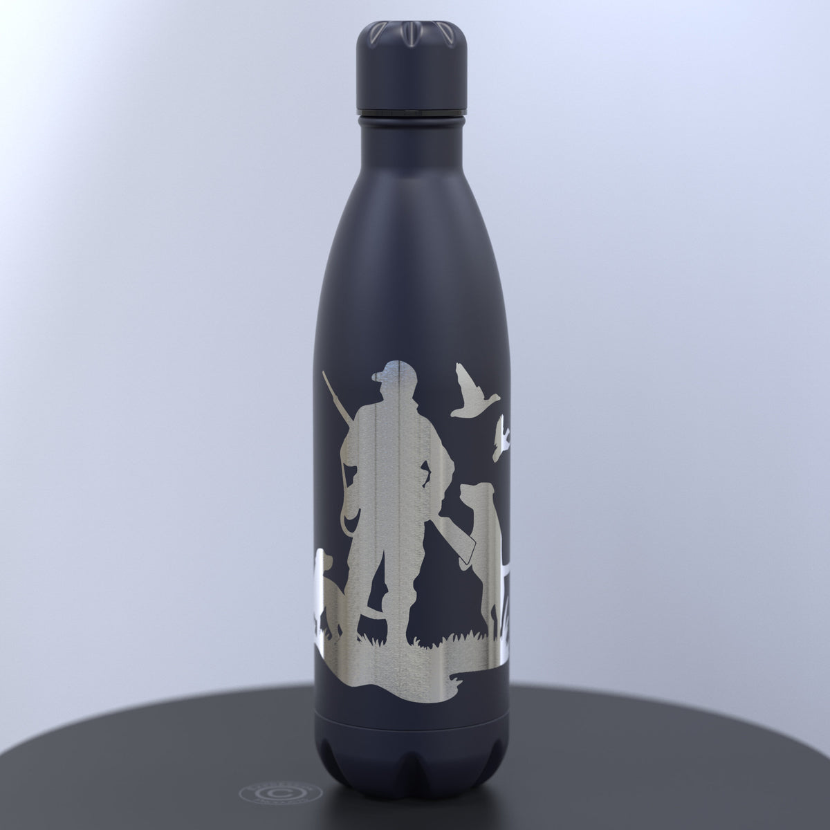A dark blue insulated water bottle with a silver-toned engraved hunting silhouette design of a man, dogs and ducks