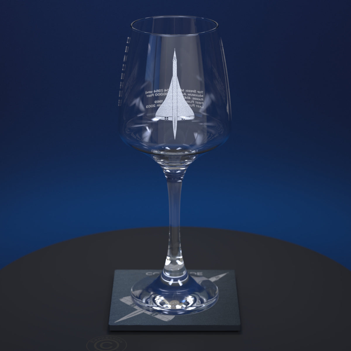 A clear stemmed wine glass with a white etched Concorde design and text on the bowl, displayed on a square slate coaster against a dark blue gradient background.