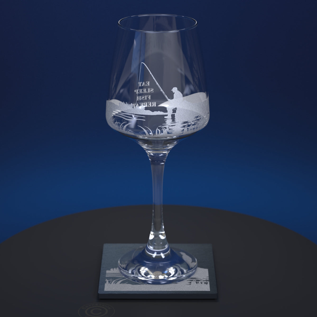 A clear glass wine glass with an etched  fishing scene and the words 'EAT SLEEP REPEAT' on the bowl, displayed on a square slate coaster against a dark blue background.